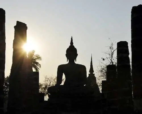 夕焼けに染まるスコータイ歴史公園。座仏像と仏塔の劇的なシルエットが、この地の神秘的な歴史を物語る。