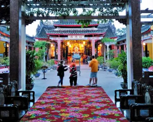 ホイアン旧市街にある美しく装飾された古代の会館内部。精巧な木造建築、鮮やかな赤い絨毯、そして輝く提灯が特徴で、観光客が歴史的な内装を探索しています。