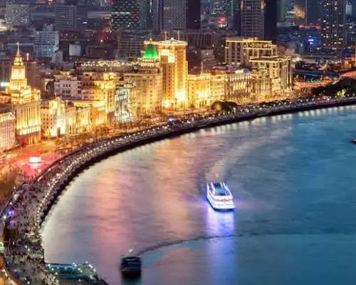 Quang cảnh từ trên cao của bờ kè Bến Thượng Hải lấp lánh và sông Hoàng Phố vào ban đêm, với các tàu du thuyền di chuyển và cuộc sống về đêm sôi động của Thượng Hải.