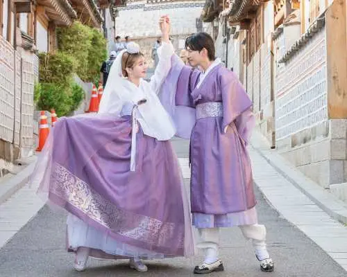 A joyful couple in matching purple Hanboks playfully interacting on a charming traditional Korean street in Seoul, perfect for a romantic Hanbok photoshoot experience.