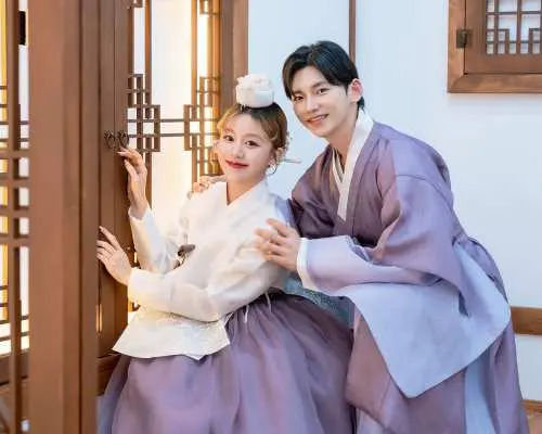 A happy couple in coordinated purple Hanboks posing inside a beautifully decorated Hanok-style studio in Seoul, capturing their memorable Hanbok photoshoot experience.