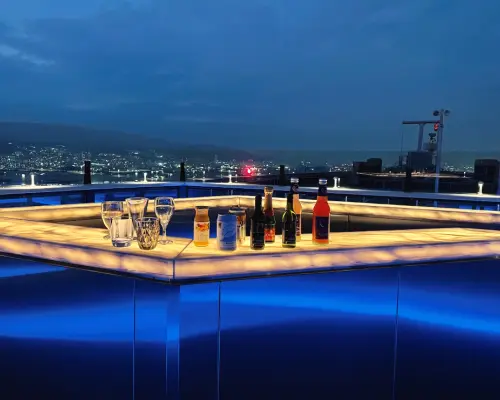神戸屋上テラス「そらふね」のバーカウンター。様々な特製ドリンクが並び、遠くには輝く神戸の街の明かりが広がり、夜のデートに最適なロケーションです。