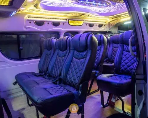 Close-up interior of a luxury chartered van in Bangkok, featuring comfortable dark quilted seats and an intricately designed ceiling with vibrant blue and yellow LED lights for a premium ride.