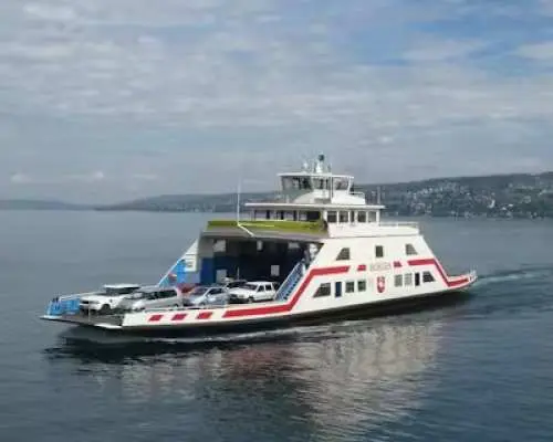 一艘大型白色汽車渡輪在平靜的蘇黎世湖上行駛，甲板上載運著車輛，體驗獨特的湖上交通。