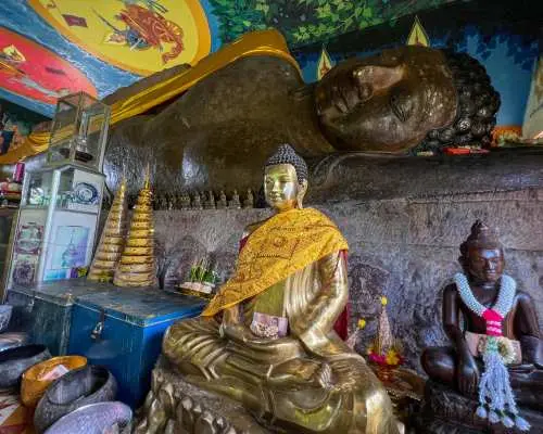 Sacred reclining Buddha statue and golden seated Buddha idol inside a temple on Phnom Kulen, Cambodia, showcasing the region's spiritual heritage.