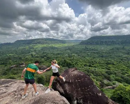 Couple enjoying the breathtaking panoramic views of the lush green landscapes and rolling hills from a rocky outcrop on Phnom Kulen, Cambodia.