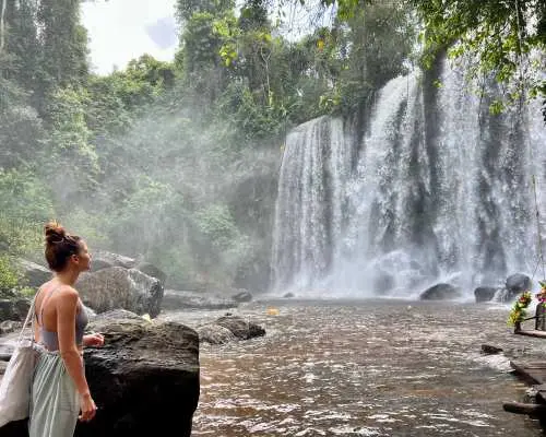 Visitor admiring the impressive waterfall at Phnom Kulen in Cambodia, surrounded by lush tropical greenery, perfect for nature exploration.