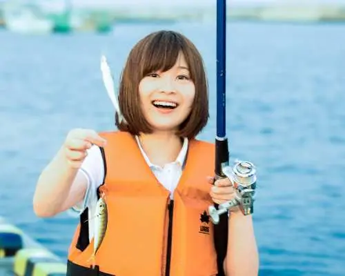A happy young woman in an orange life vest proudly displays her fresh catch during a relaxing dock fishing experience in Sasebo, Nagasaki, enjoying the success.