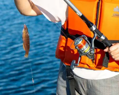 Close-up of a participant in an orange life vest holding a fishing rod with a small fish on the line, showcasing a successful catch in Sasebo, Nagasaki, emphasizing safety.