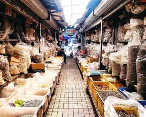 中山【沙崗墟】百年煙火市集巷道，兩旁小攤販擺滿各式商品，展現當地熱鬧的傳統市集氛圍，是團體旅遊的亮點。