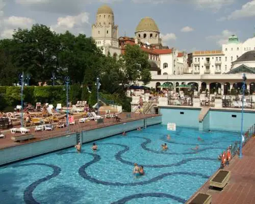 蓋勒特溫泉浴場戶外蜿蜒設計的溫泉池，遊客在樹木與古老建築環繞下休憩，享受布達佩斯獨特的戶外溫泉文化。