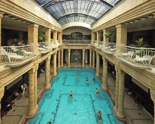 蓋勒特溫泉浴場華麗的室內泳池大廳，古典柱廊、精美陽台與挑高玻璃屋頂設計，呈現宏偉的布達佩斯溫泉藝術建築。