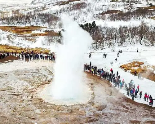アイスランドのゴールデンサークルでゲイシール間欠泉が壮大に噴出。雪景色の中、観光客がこの冬の地熱の驚異を体験しています。