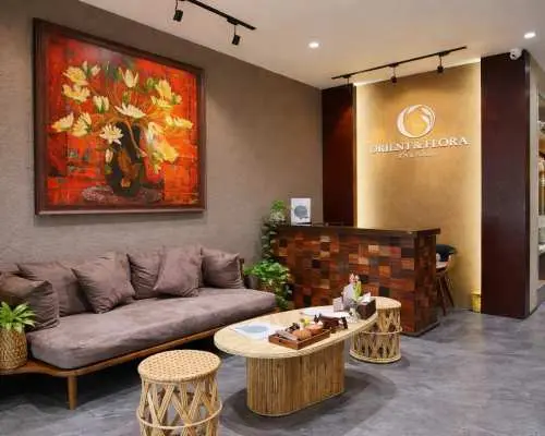 La Flora Spa reception area, where a staff member in Ao Dai warmly welcomes a customer, introducing Hanoi's spa and massage services with professional and passionate hospitality.