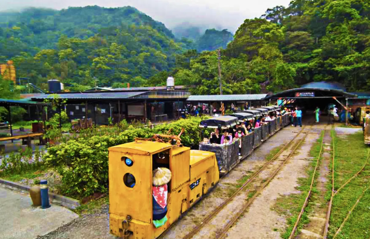 Unique 'One-Eyed Train' carrying visitors on tracks through green mountains at New Pingxi Coal Mine Museum, for a historical mining experience.
