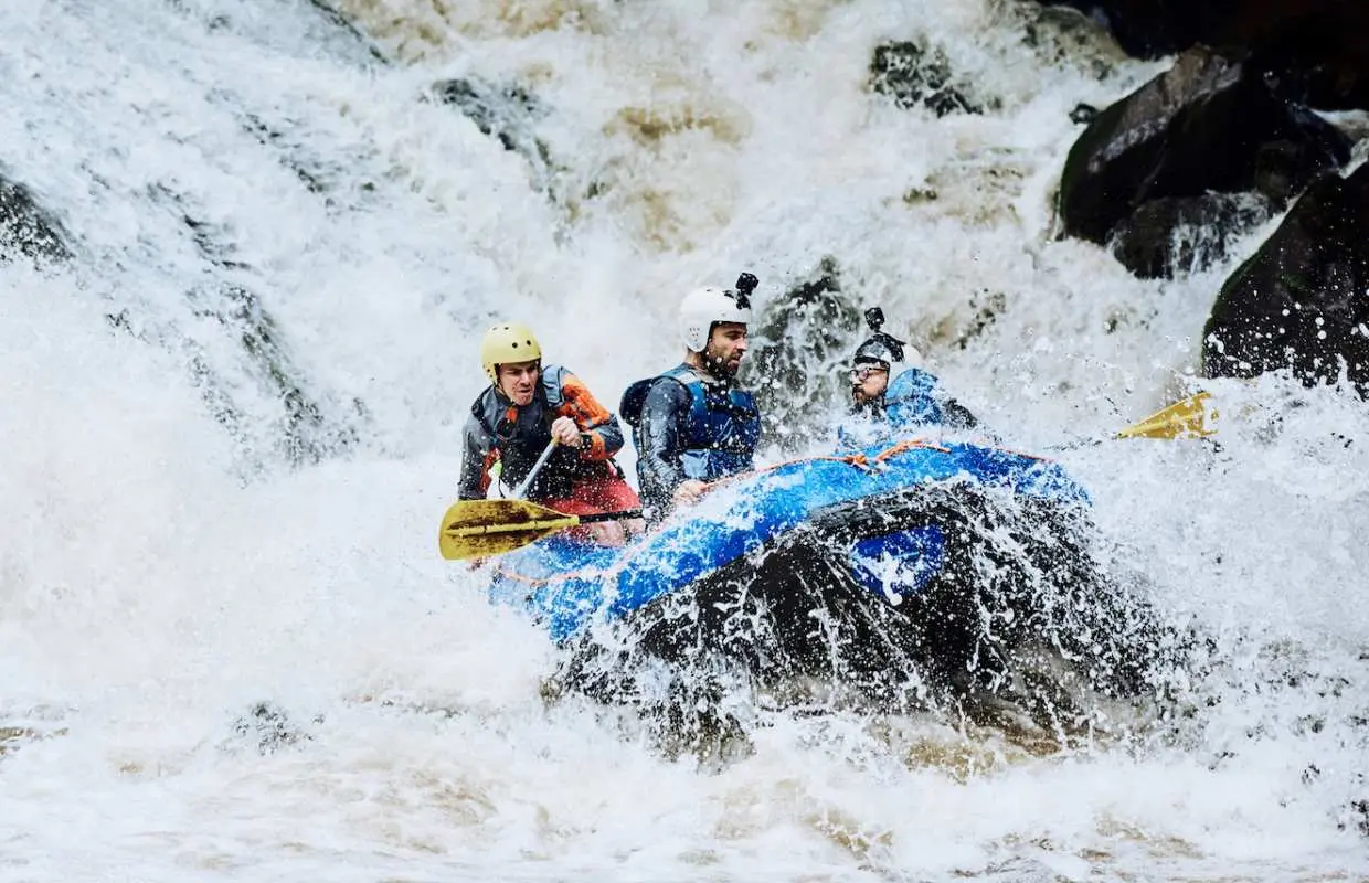 Thrilling whitewater rafting in Phuket, with three adventurers in a blue raft, wearing helmets and life vests, paddling through intense rapids.
