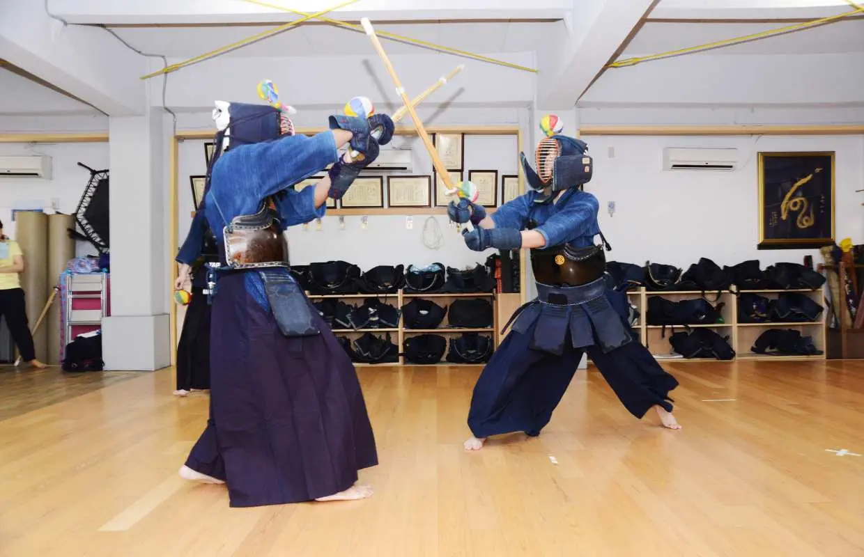 Two participants in full kendo armor spar with bamboo swords in a Tokyo dojo, practicing combat and learning the spirit of samurai martial arts.