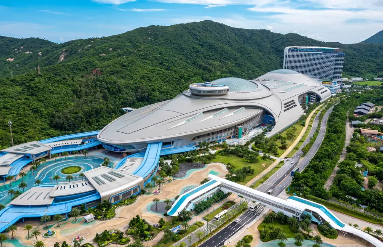珠海長隆飛船樂園外觀空拍圖，巨型飛船造型建築坐落於翠綠山景與道路旁。