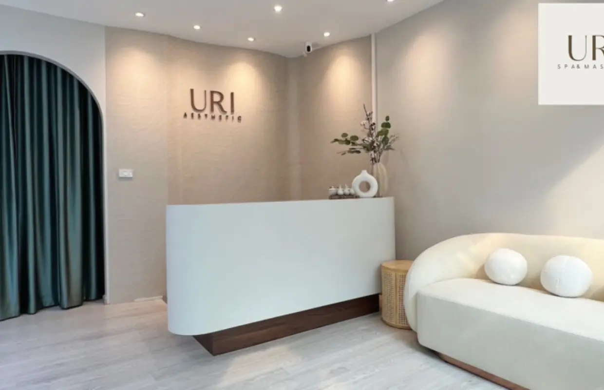 URI Spa & Massage Asok 分店的現代接待區，設有弧形櫃檯、舒適梳化和綠色窗簾，營造寧靜氛圍，歡迎您享受放鬆的水療體驗。