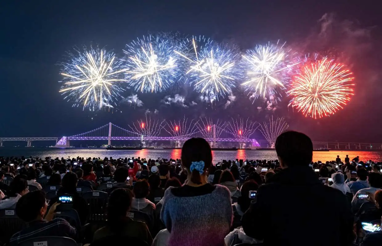 廣安里海水浴場的觀眾正仰望夜空中，2025釜山煙火節在廣安大橋上方綻放多樣璀璨煙火。