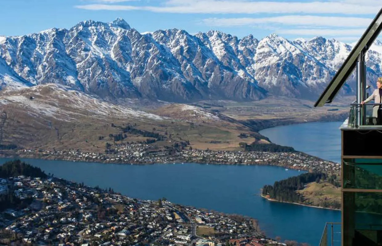 Visitors enjoy panoramic views of Queenstown, Lake Wakatipu, and the majestic snow-capped mountains from the Skyline observation deck in New Zealand.