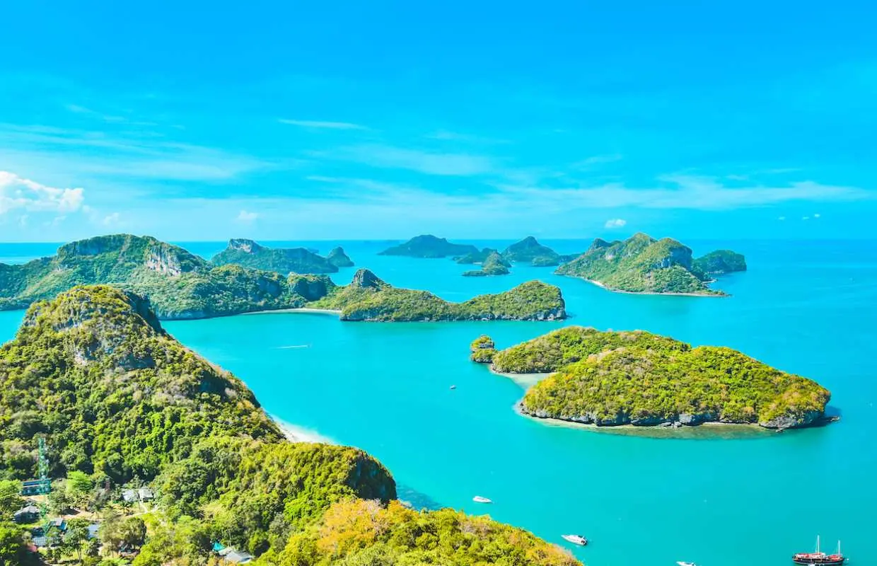 Aerial view of Angthong National Marine Park from Koh Samui, featuring lush green limestone islands scattered across vibrant turquoise waters under a clear blue sky, highlighting the stunning seascape.