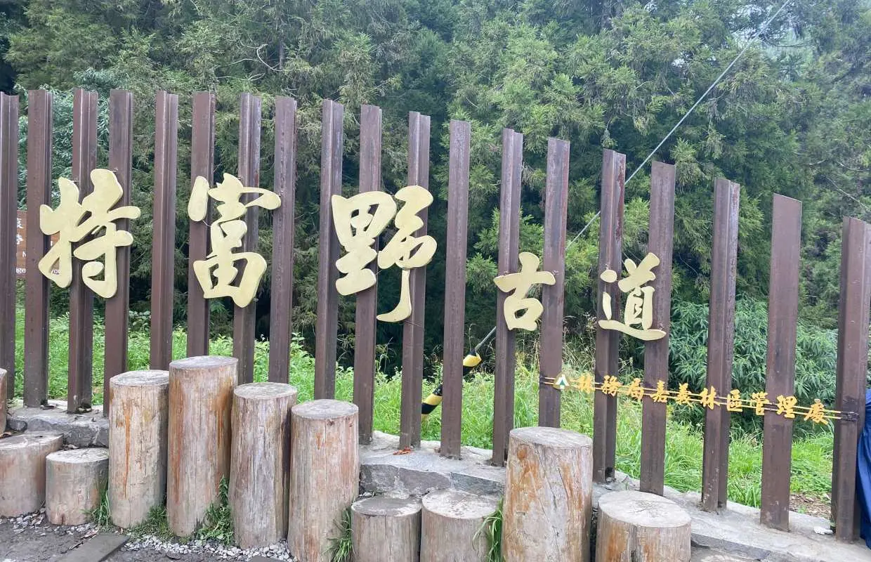 Alishan's Tefuye Ancient Trail entrance sign, with golden characters on a wooden fence amidst lush greenery, marking the start of a scenic historic mountain path.