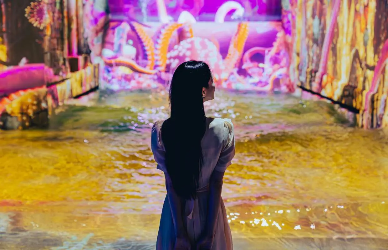 ในสวนสื่อน้ำ Jeju Waterworld หญิงสาวหันหลังให้กล้อง ยืนอยู่บนผืนน้ำสีส้มสุดแฟนตาซี ล้อมรอบด้วยภาพฉายหนวดปลาหมึกและสิ่งมีชีวิตใต้ทะเล สร้างบรรยากาศลึกลับของโลกใต้สมุทร