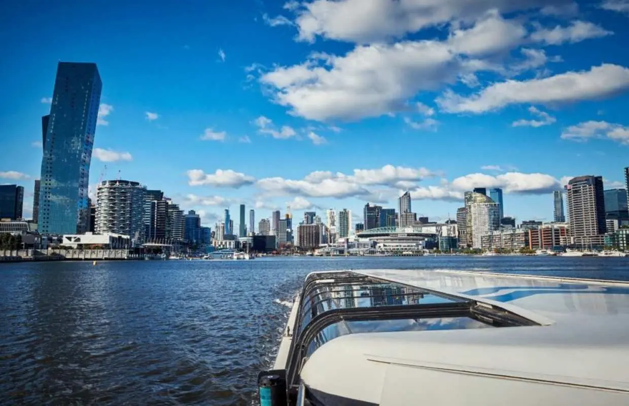 雅拉河观光游船驶向墨尔本市中心，展示城市天际线与现代建筑，蓝天白云下的最佳游览视角。