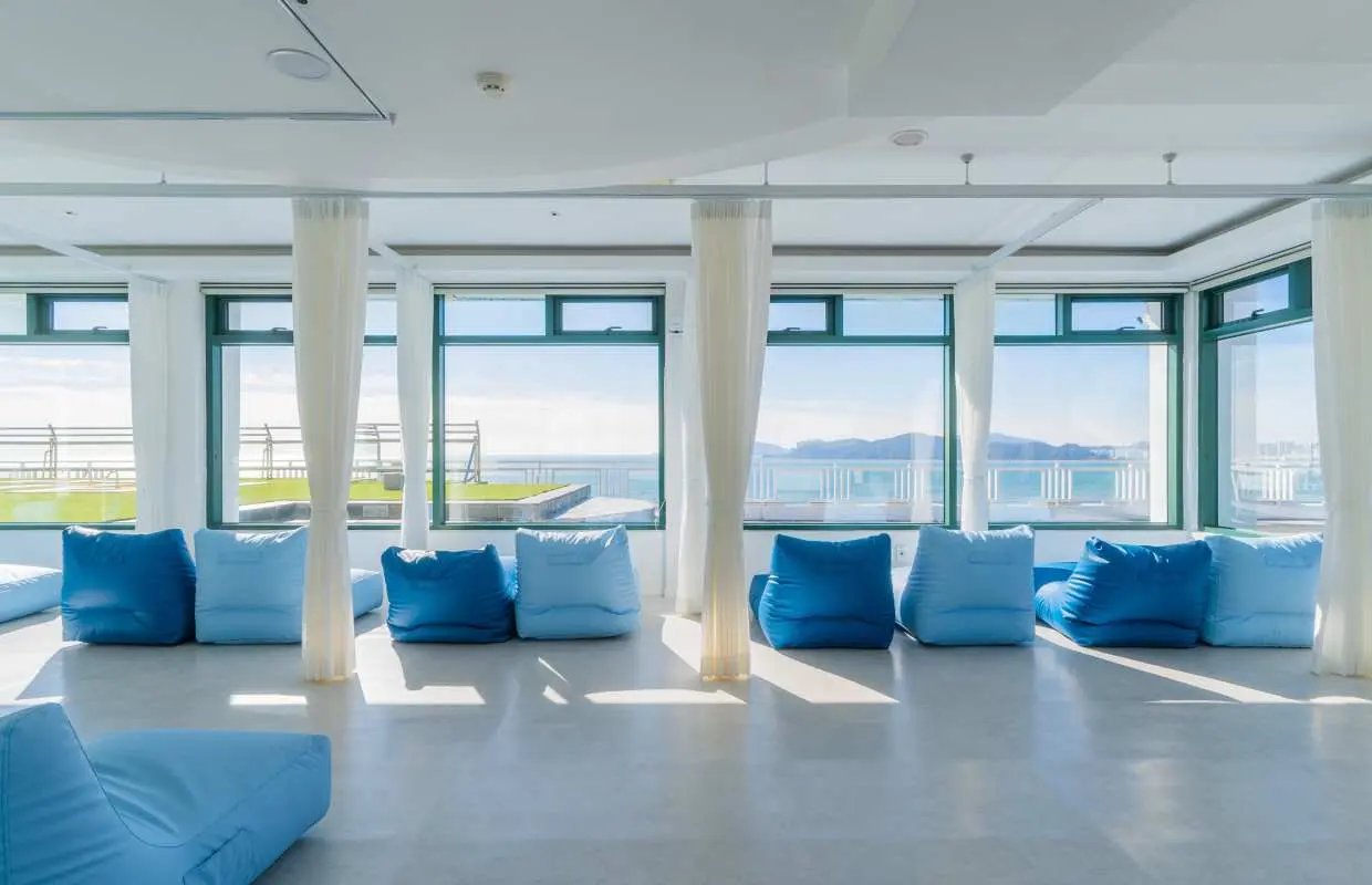 Busan Haeundae HILL SPA's spacious, bright relaxation area features comfortable blue bean bag chairs and floor-to-ceiling windows offering panoramic ocean views, perfect for unwinding.