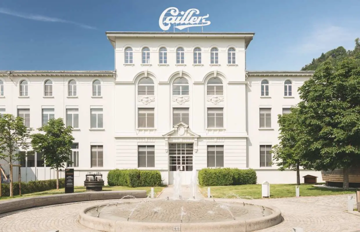 The majestic exterior of Maison Cailler chocolate factory in Broc, Switzerland, with a beautiful fountain, a renowned landmark for Swiss chocolate experiences.