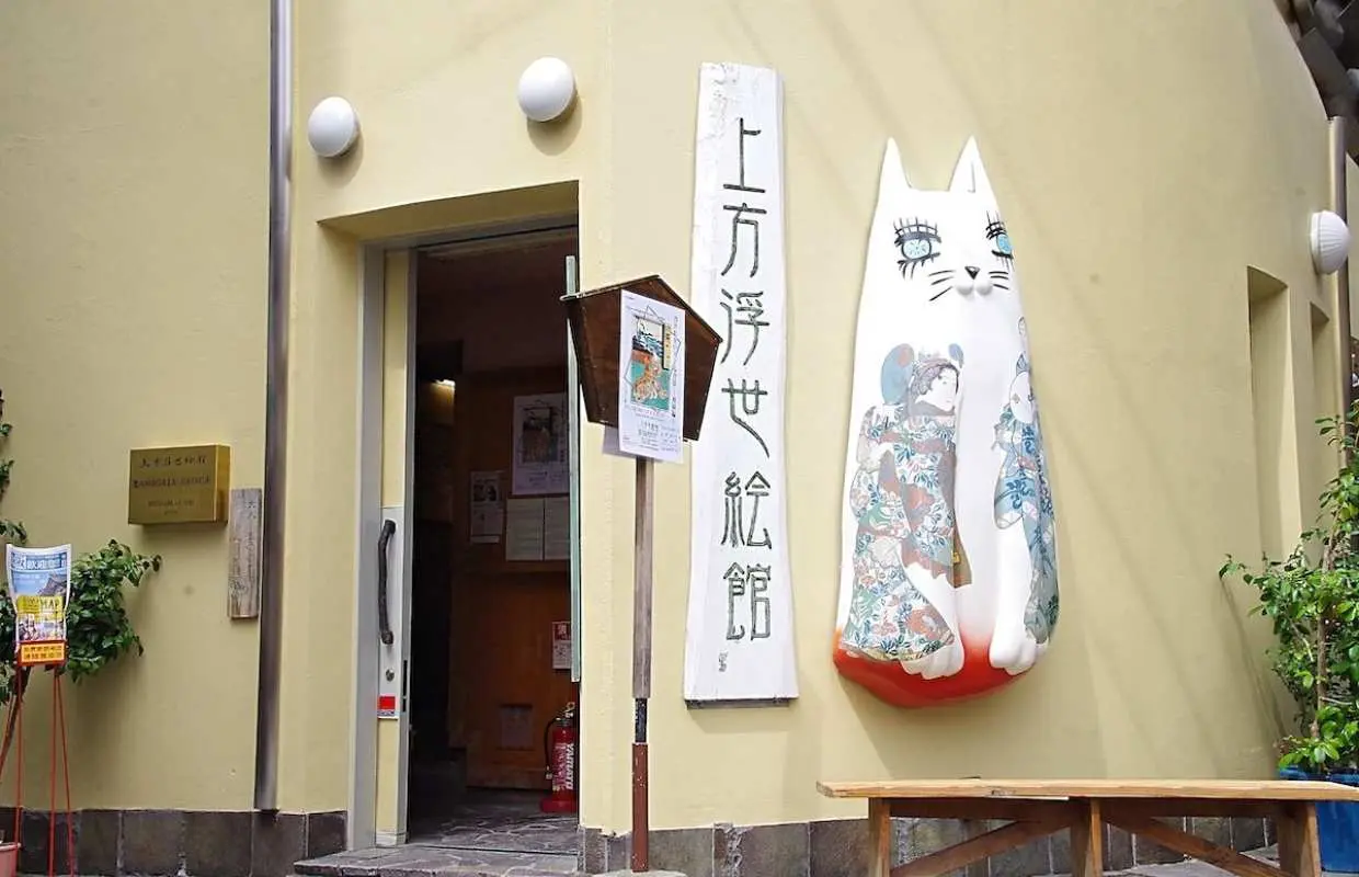 大阪上方浮世繪館入口，黃色建築搭配「上方浮世繪館」招牌與大型貓咪雕塑，展現獨特藝術氛圍。