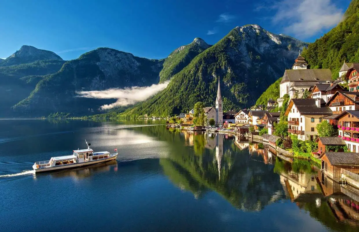 오스트리아 할슈타트 호수 위를 유람선이 지나가는 모습. 에메랄드빛 호수와 그림 같은 마을, 웅장한 산이 어우러진 아름다운 풍경을 담은 할슈타트 차량투어.