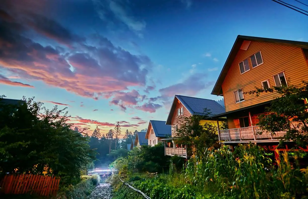 多林车站附近山间的木屋民宿，沐浴在夕阳余晖中，粉橘色的云彩装点天空，提供嘉义包车一日游的宁静住宿氛围。