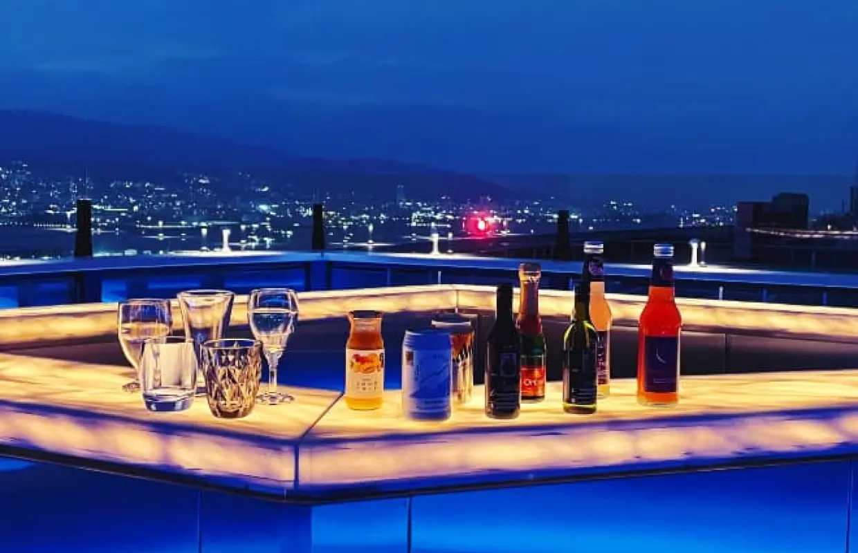 神戸屋上テラス「そらふね」の夜景。ライトアップされたスタイリッシュなバーカウンターにドリンクが並び、背景には神戸港のロマンチックな夜景が広がります。