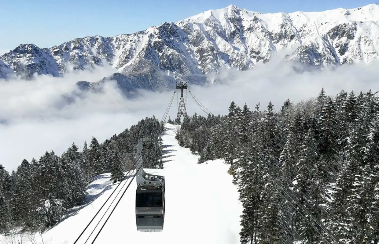 Shin-Hotaka double-decker ropeway cable car ascending through snow-covered Northern Japan Alps, amidst frost-covered trees and majestic cloud-shrouded peaks.