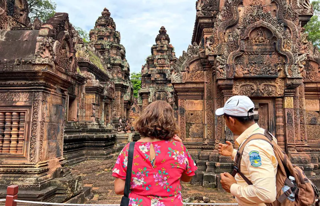 Tourist with guide exploring the intricately carved red sandstone temples of Banteay Srei in Siem Reap, Cambodia, highlighting ancient Khmer artistry.