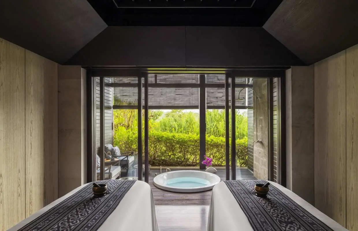 Luxurious indoor spa room at Raffles Bali, featuring two massage beds facing an outdoor plunge pool and lush tropical greenery, offering a serene and tranquil spa experience.