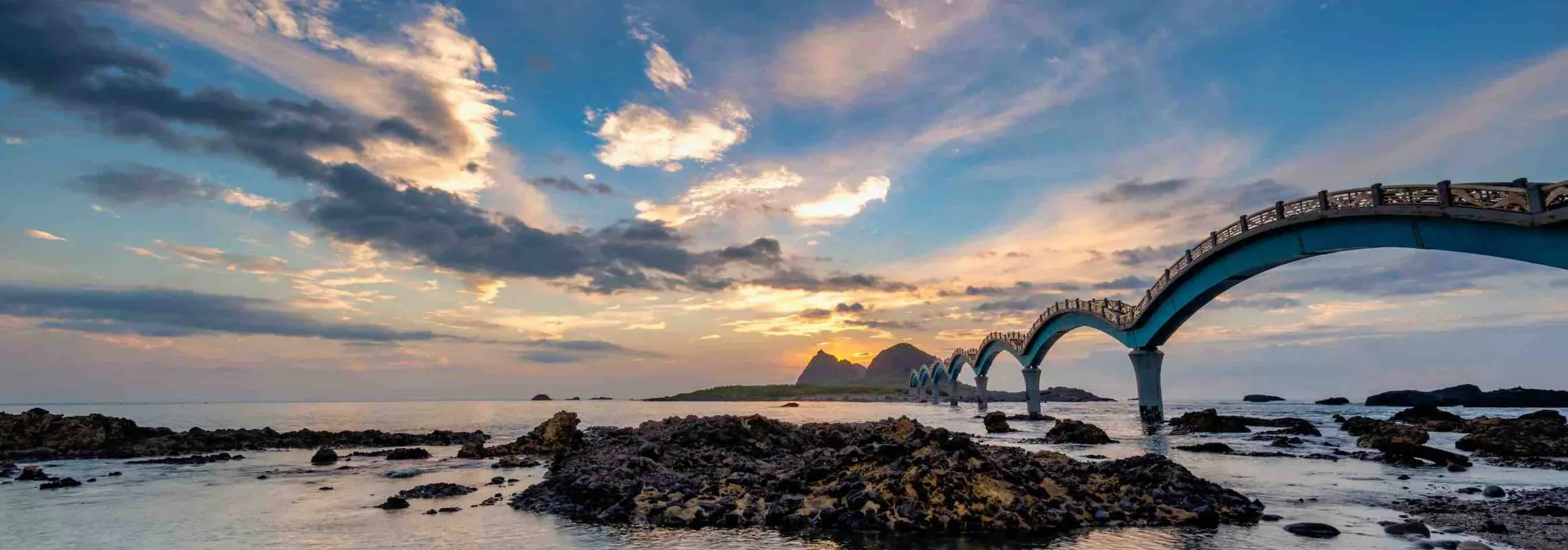 台東三仙台地標八拱橋在夕陽餘暉下，藍粉色天空倒映海面，展現壯麗海岸線與獨特自然景觀，遊客可漫步橋上欣賞美景。