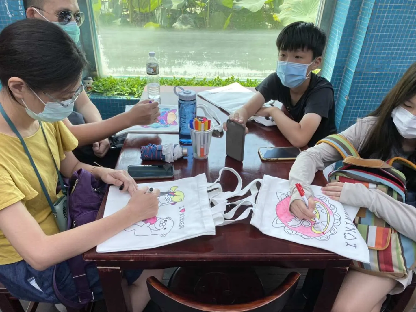遊客在金門的DIY工坊內專心彩繪風獅爺帆布袋，桌上擺放著多款個人化圖案，享受手作樂趣，打造獨特伴手禮。