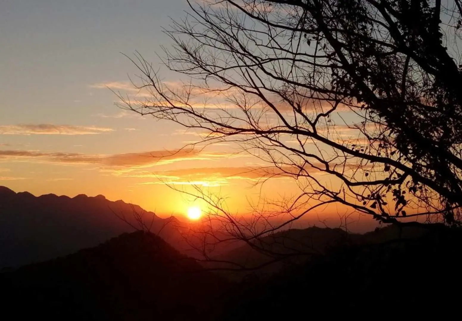 新北桃園東滿步道套票，金黃夕陽餘暉灑落滿月圓與東眼山的山巒，樹影剪影增添秋季健行步道之美。