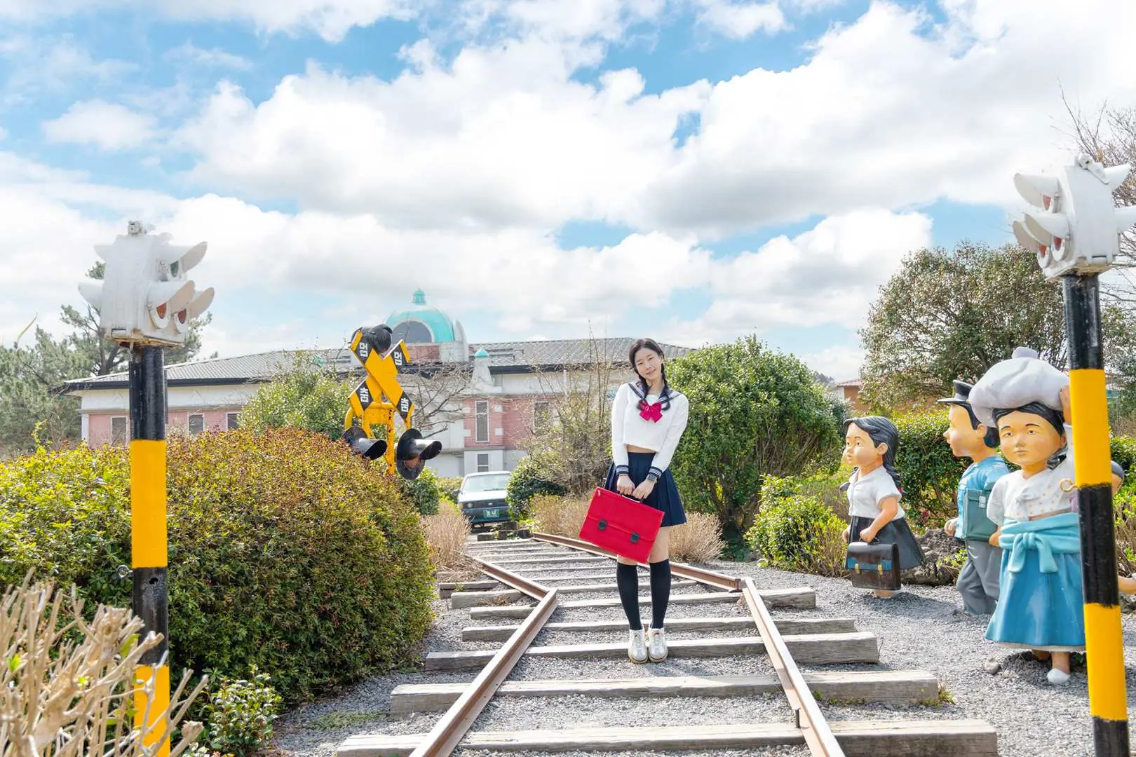 濟州仙女與樵夫主題公園，穿著復古校服的女孩站在舊鐵道上，一旁有可愛的古老人物模型，重現50-80年代懷舊場景。