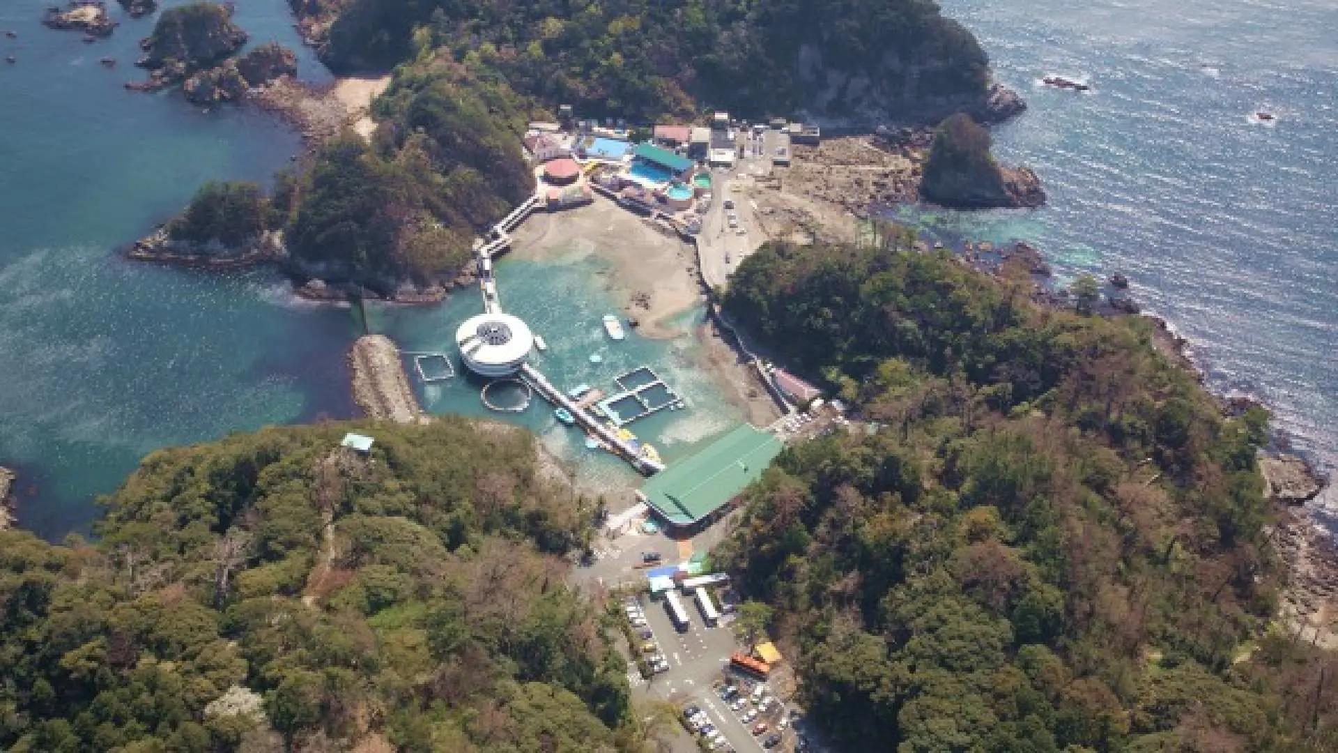 静岡県下田海中水族館の壮大な空撮パノラマ。下田湾に浮かぶユニークな姿は、緑豊かな丘と紺碧の海に囲まれ、自然との共存を象徴しています。