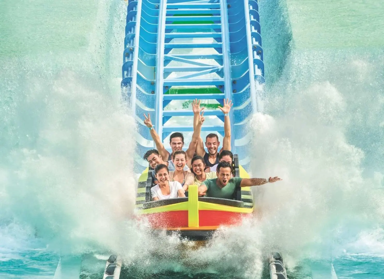 Enthusiastic visitors on the Desaru Coast Adventure Waterpark's water coaster, arms raised in excitement as their boat splashes down, creating a huge wave of water.