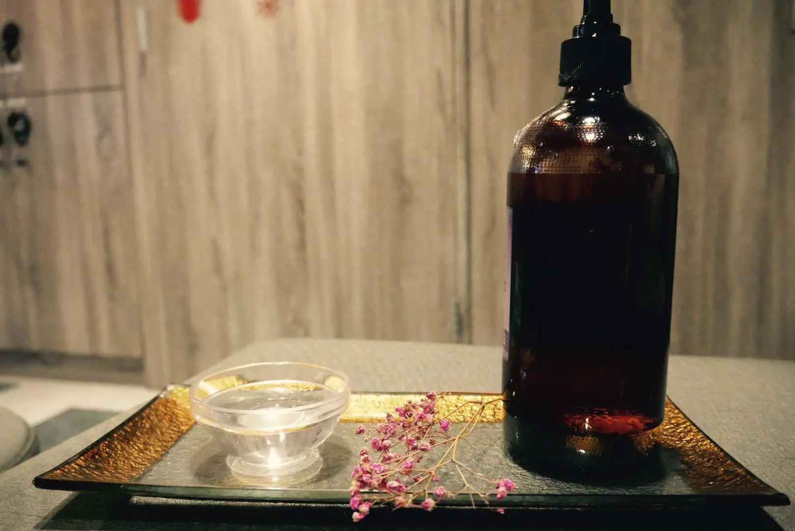 An essential oil bottle, a water bowl, and dried flowers arranged on a tray in a massage room at Taipei's Xuanwu Wellness Center, prepared for a relaxing full body massage.
