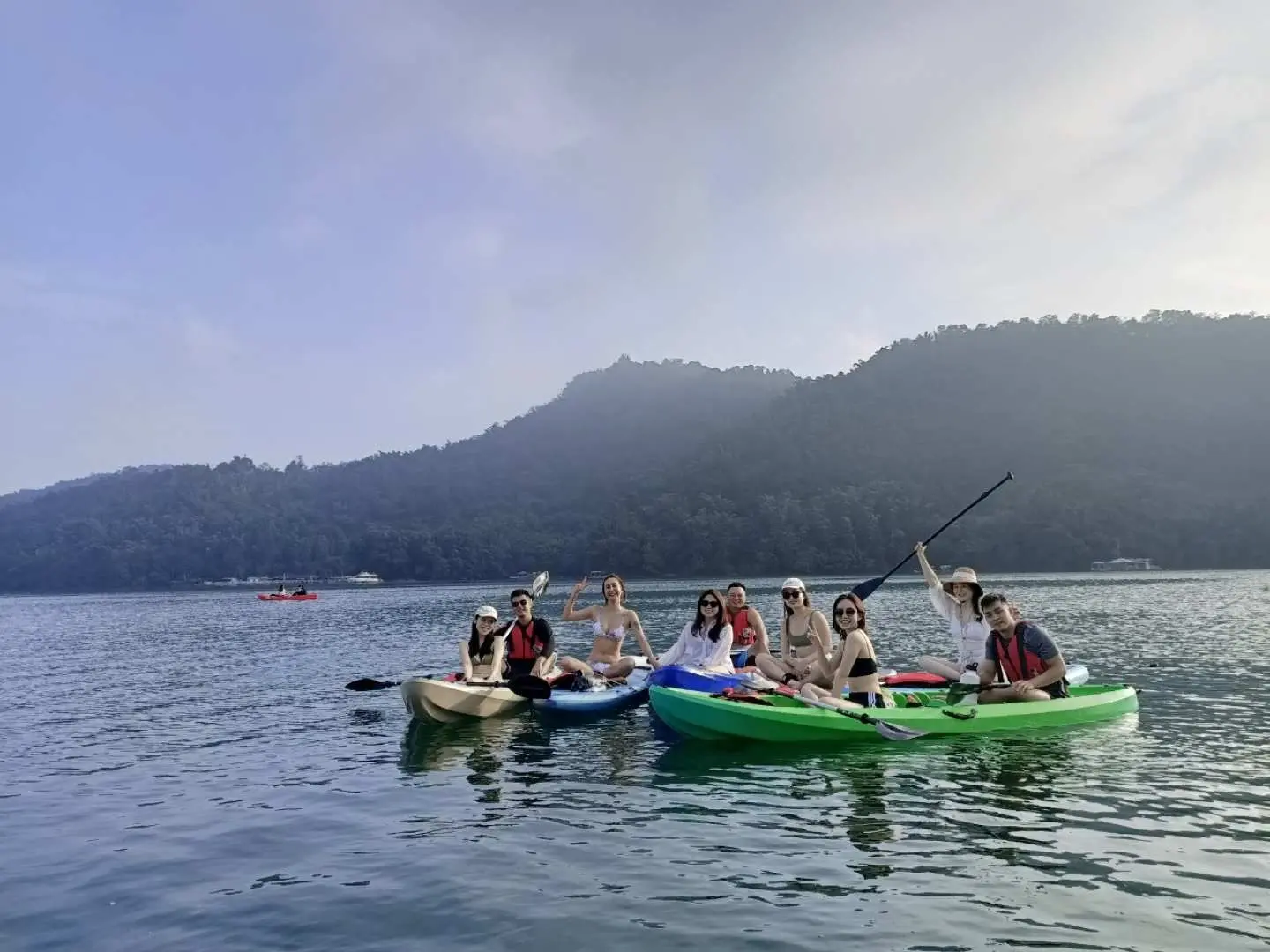 Friends enjoying kayaking and SUP paddleboarding at Sun Moon Lake, Nantou, experiencing water activities together and admiring the scenic lakeside mountains.