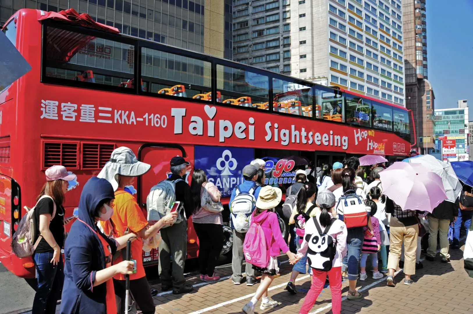 大批旅客在台北市區的雙層觀光巴士站牌前等候上車，體驗隨上隨下、輕鬆便捷的城市觀光方式。