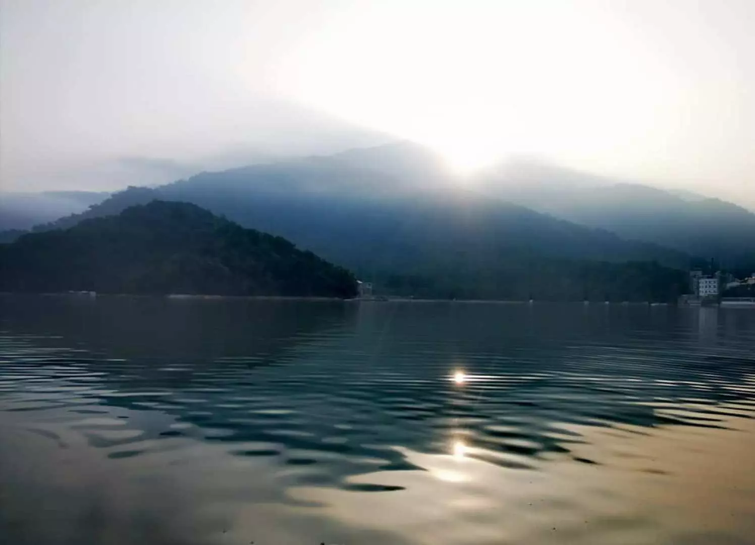日月潭湖面在晨曦或夕陽下波光粼粼，遠方山巒雲霧繚繞，展現南投SUP瑜珈體驗的寧靜自然美景。