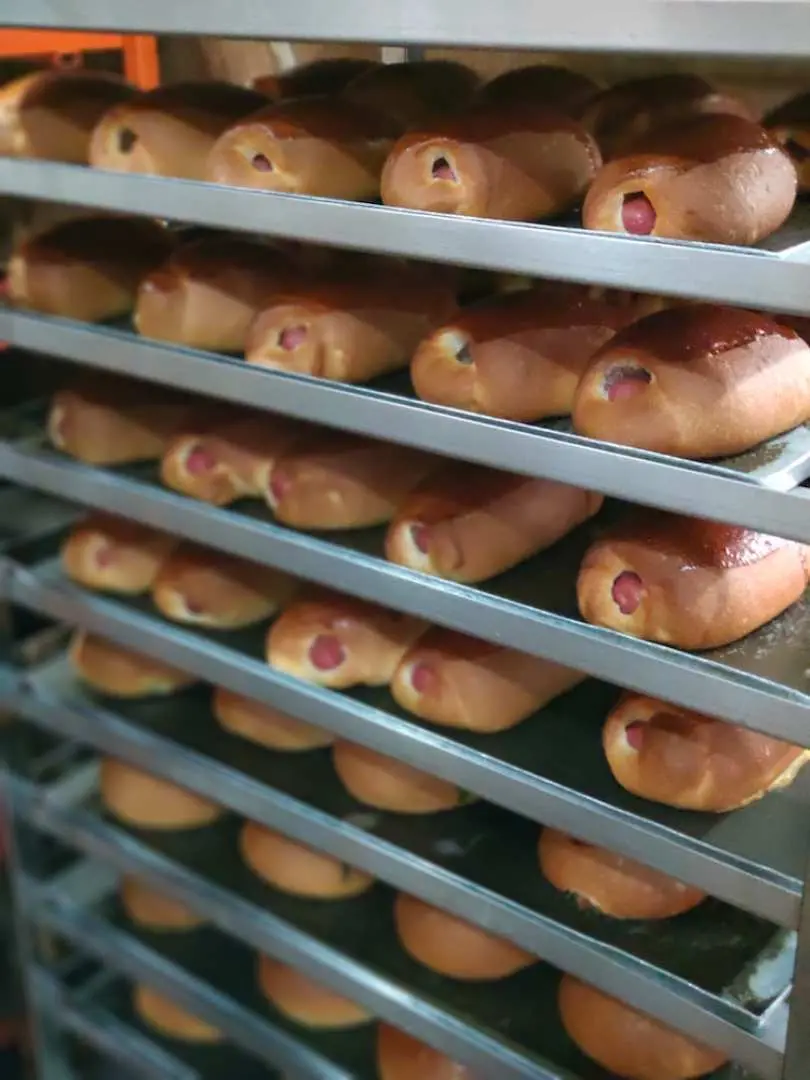 Shelves filled with rows of golden-brown sausage buns, a common and delicious sight in Singapore's traditional bakeries awaiting visitors on a cultural food tour.