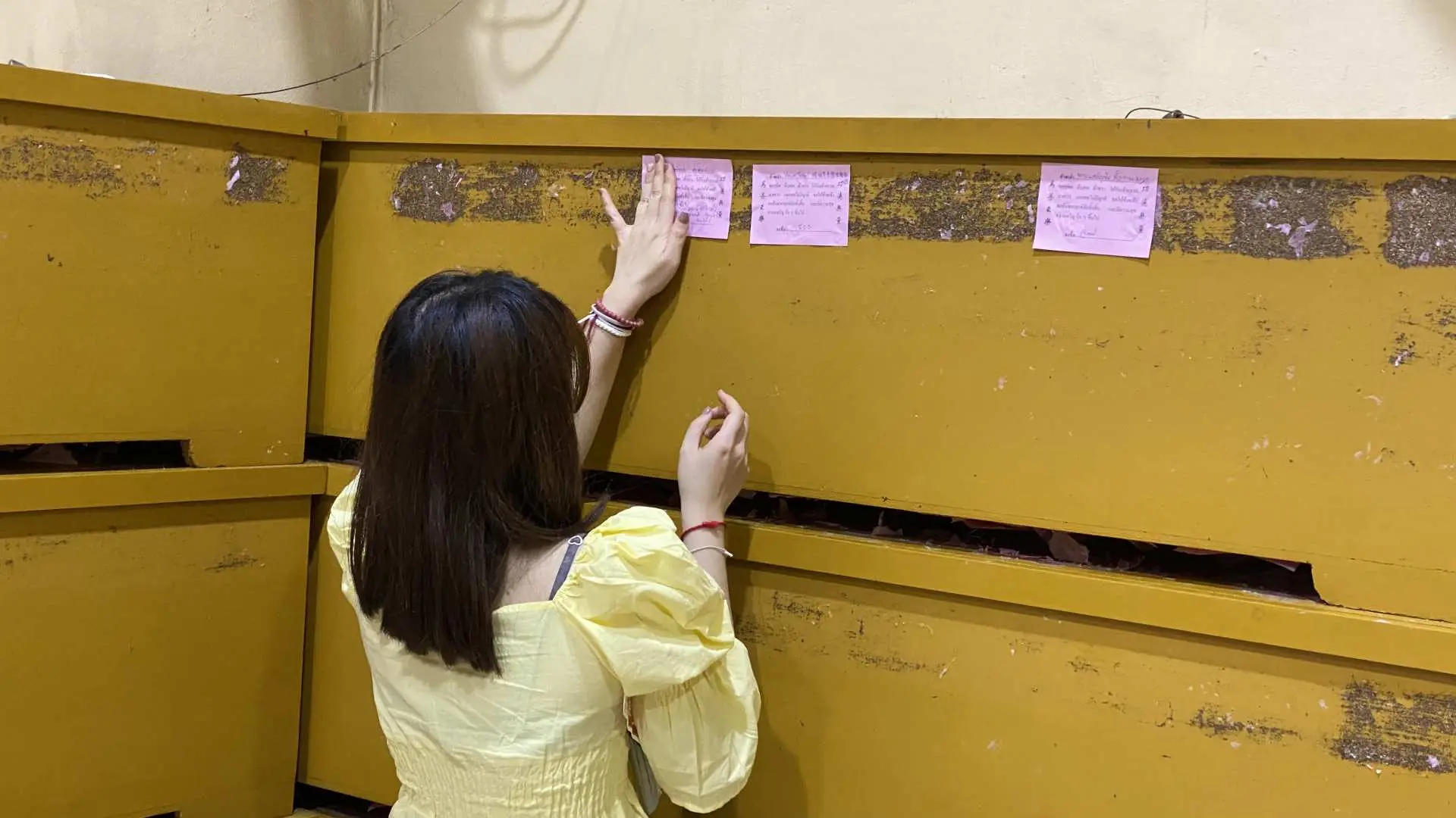 A volunteer at Bangkok's Ruamkatanyu Foundation carefully attaching a proxy donor's merit slip onto a coffin box, symbolizing the transfer of good intentions.